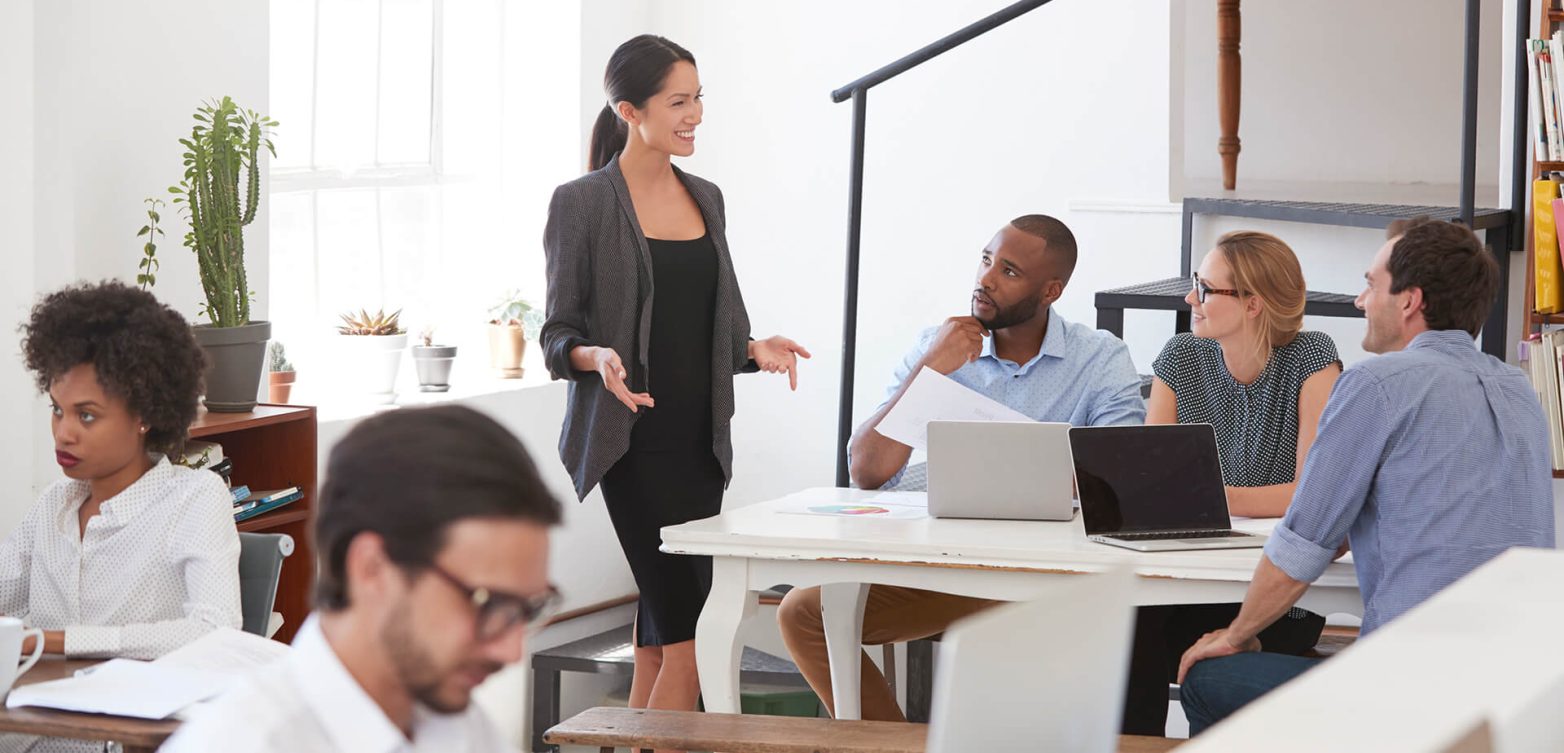 woman-talking-to-colleagues-at-a-desk-in-open-plan-PV79E8M.jpg